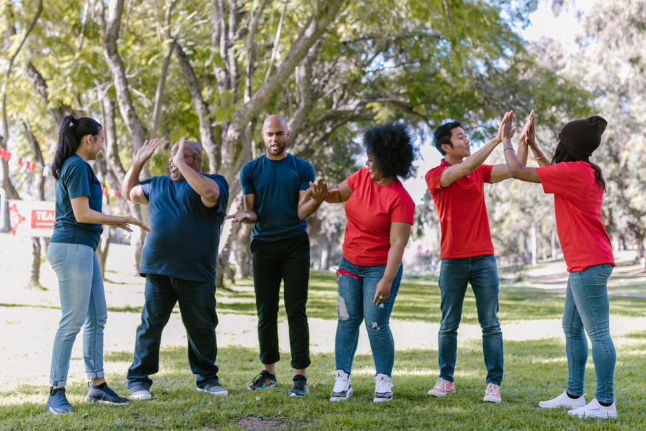 Home Multicultural team engaging in outdoor team building exercises in a park setting.