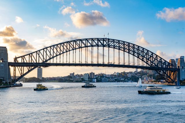 Picturesque view of Sydney Harbour Bridge during sunset with ferries and sailboats on the water.