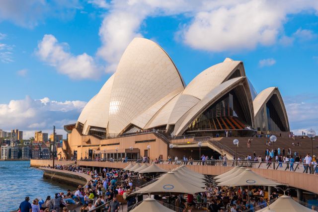 The iconic Sydney Opera House with a bustling crowd and vibrant sky.